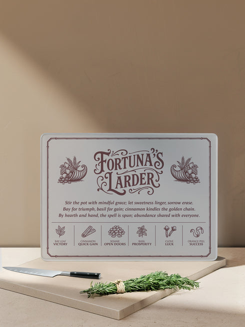 A rectangular tempered glass cutting board with a lightly textured, hygienic surface, rounded corners, and four rubber feet for stability. Printed in deep maroon line art, it features a Victorian-style border and twin cornucopias flanking the title “Fortuna’s Larder.” Below, a poetic spell invokes abundance, followed by six herb correspondences: Bay Leaf Victory, Cinnamon Quick Gain, Sesame Open Doors, Basil Prosperity, Clove Luck, and Orange Peel Success, for kitchen witches and magical cooks.