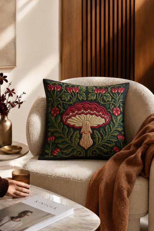 Square decorative pillow cover with a deep midnight navy ground and a symmetrical Art Nouveau botanical design rendered in a faux embroidery style. A large central mushroom anchors the composition, its scarlet ruffled cap fanning over cream and ivory gills above a pale peach stem. Curling green ferns, leafy vines, crimson flower buds, and small red blossoms frame the toadstool on every side. The printed satin-stitch detailing mimics hand-stitched thread across the entire face of the cover.