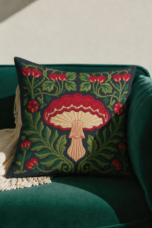 Square decorative pillow cover with a deep midnight navy ground and a symmetrical Art Nouveau botanical design rendered in a faux embroidery style. A large central mushroom anchors the composition, its scarlet ruffled cap fanning over cream and ivory gills above a pale peach stem. Curling green ferns, leafy vines, crimson flower buds, and small red blossoms frame the toadstool on every side. The printed satin-stitch detailing mimics hand-stitched thread across the entire face of the cover.