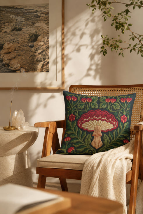 Square decorative pillow cover with a deep midnight navy ground and a symmetrical Art Nouveau botanical design rendered in a faux embroidery style. A large central mushroom anchors the composition, its scarlet ruffled cap fanning over cream and ivory gills above a pale peach stem. Curling green ferns, leafy vines, crimson flower buds, and small red blossoms frame the toadstool on every side. The printed satin-stitch detailing mimics hand-stitched thread across the entire face of the cover.