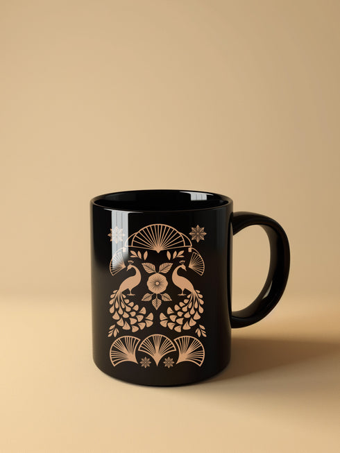 A black ceramic mug featuring an Art Deco-inspired design in rose gold. The symmetrical pattern shows two peacocks with fan-shaped tails, surrounded by ginkgo fan motifs and floral elements. The central design includes a stylized flower with leaves, and decorative stars accent the composition. The mug has a classic C-shaped handle.