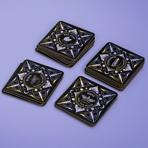 A 4-piece wealth-themed coaster set featuring intricate, gold and black designs with iridescent accents. Each coaster is dedicated to a different herb or spice, including basil, bay leaf, cinnamon, and mint, each symbolizing prosperity, abundance, riches, and wealth. The designs feature celestial motifs and geometric patterns, adding a mystical and luxurious touch to the coasters.