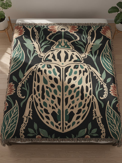 Jacquard woven 100% cotton blanket from Grimoire and Goblet featuring a detailed central beetle entomology motif and vintage botanical floral accents. The textile displays a rich woven texture with a fringe border in a dark academia palette of charcoal black, ochre, and rust. This heirloom-quality gothic tapestry functions as a decorative wall hanging or luxury throw for moody library and study interiors, showcasing high-fidelity thread-work and the brand's sorcerous aesthetic.