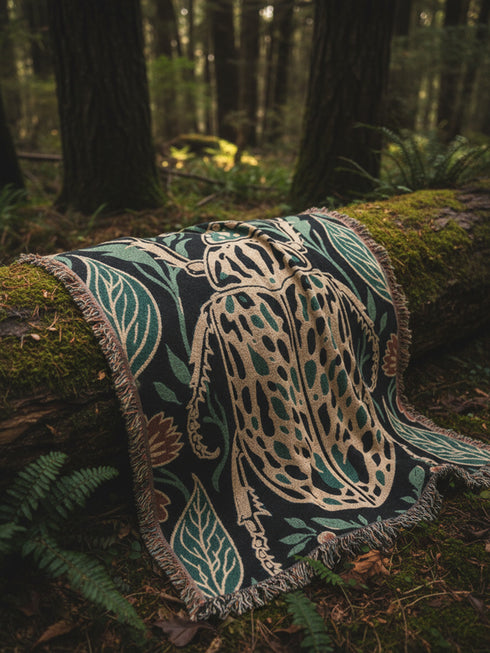Jacquard woven 100% cotton blanket from Grimoire and Goblet featuring a detailed central beetle entomology motif and vintage botanical floral accents. The textile displays a rich woven texture with a fringe border in a dark academia palette of charcoal black, ochre, and rust. This heirloom-quality gothic tapestry functions as a decorative wall hanging or luxury throw for moody library and study interiors, showcasing high-fidelity thread-work and the brand's sorcerous aesthetic.