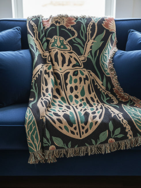 Jacquard woven 100% cotton blanket from Grimoire and Goblet featuring a detailed central beetle entomology motif and vintage botanical floral accents. The textile displays a rich woven texture with a fringe border in a dark academia palette of charcoal black, ochre, and rust. This heirloom-quality gothic tapestry functions as a decorative wall hanging or luxury throw for moody library and study interiors, showcasing high-fidelity thread-work and the brand's sorcerous aesthetic.
