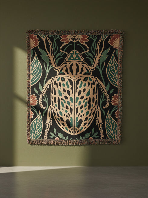 Jacquard woven 100% cotton blanket from Grimoire and Goblet featuring a detailed central beetle entomology motif and vintage botanical floral accents. The textile displays a rich woven texture with a fringe border in a dark academia palette of charcoal black, ochre, and rust. This heirloom-quality gothic tapestry functions as a decorative wall hanging or luxury throw for moody library and study interiors, showcasing high-fidelity thread-work and the brand's sorcerous aesthetic.