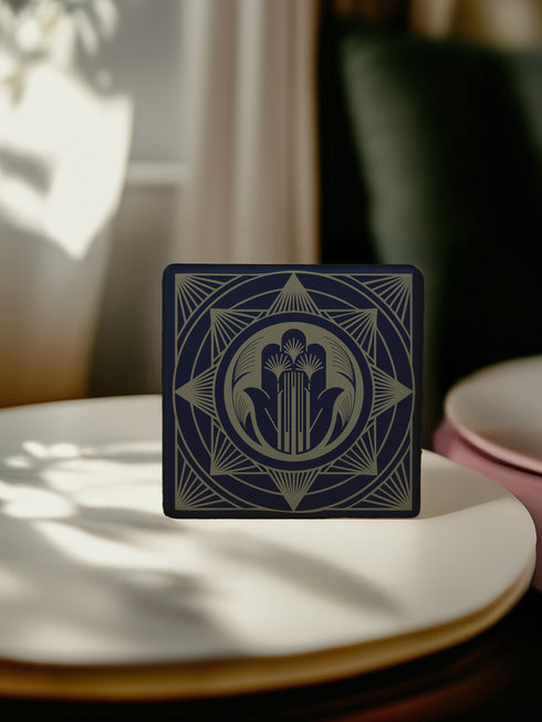 A black and gold ceramic coaster featuring an intricate Hamsa Hand design with celestial and art deco influences.