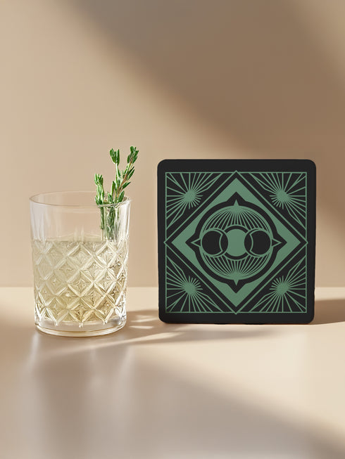 A black and emerald green ceramic coaster featuring a triple moon motif with celestial art deco sunbursts.