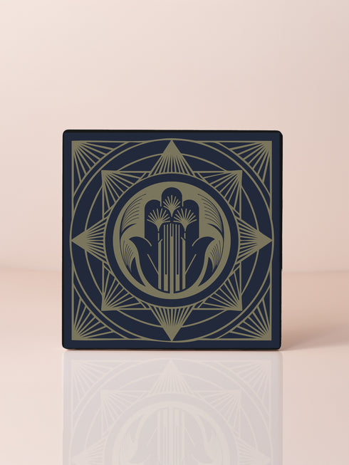 A black and gold ceramic coaster featuring an intricate Hamsa Hand design with celestial and art deco influences.