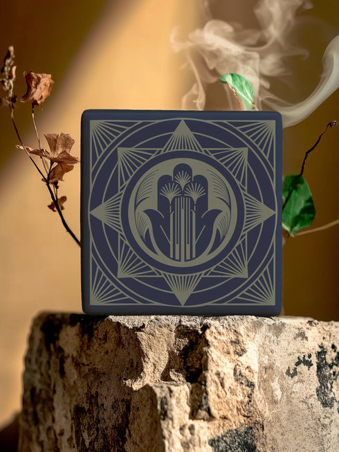 A black and gold ceramic coaster featuring an intricate Hamsa Hand design with celestial and art deco influences.