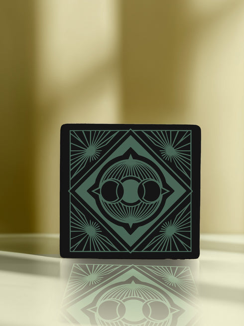 A black and emerald green ceramic coaster featuring a triple moon motif with celestial art deco sunbursts.