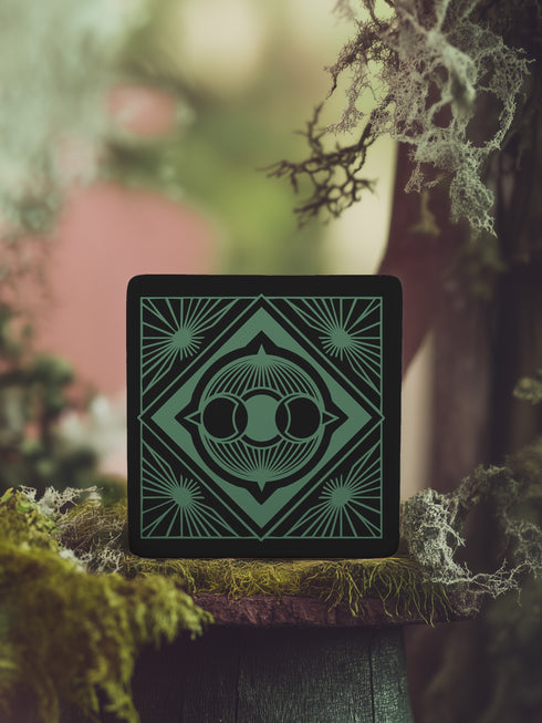 A black and emerald green ceramic coaster featuring a triple moon motif with celestial art deco sunbursts.