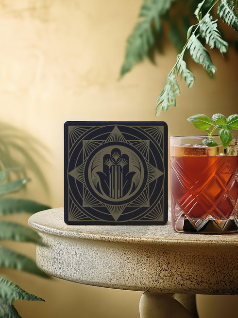 A black and gold ceramic coaster featuring an intricate Hamsa Hand design with celestial and art deco influences.