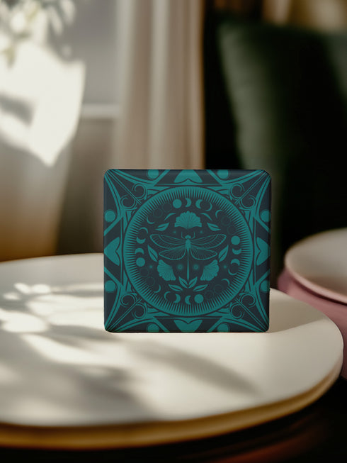 Square ceramic coaster featuring a detailed emerald green dragonfly illustration centered in a medallion, surrounded by moon phases and Art Nouveau patterns on a dark background.