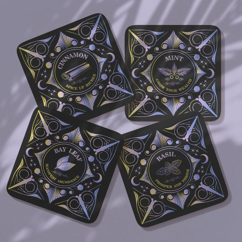 Four black square coasters with shimmering holographic designs. Each features a different herb (Mint, Basil, Bay Leaf, Cinnamon) and associated wealth-attracting phrase in ornate lettering.
