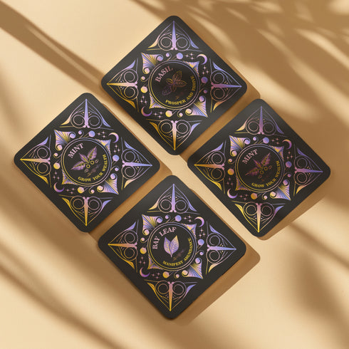 A 4-piece wealth-themed coaster set featuring intricate, gold and black designs with iridescent accents. Each coaster is dedicated to a different herb or spice, including basil, bay leaf, cinnamon, and mint, each symbolizing prosperity, abundance, riches, and wealth. The designs feature celestial motifs and geometric patterns, adding a mystical and luxurious touch to the coasters.