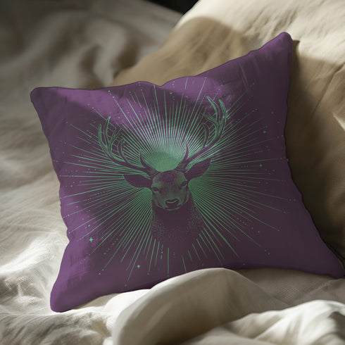 A pillow cover with a bold stag's head emerging from an ethereal burst of mint green rays against deep purple fabric. Delicate starbursts scatter around the deer, creating a celestial effect.