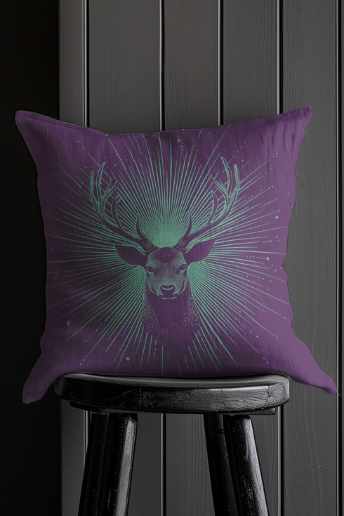 A pillow cover with a bold stag's head emerging from an ethereal burst of mint green rays against deep purple fabric. Delicate starbursts scatter around the deer, creating a celestial effect.