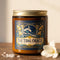 A 9 oz amber glass jar candle with a brushed gold screw lid and a wraparound deep navy label. The label shows a cresting wave beneath a crescent moon, framed by two classical columns and an arched window, with golden art nouveau freesias climbing both sides on teal stems, all inside a fine gold border. A cream banner reads The Tidal Oracle, with Grimoire & Goblet above and Sea Salt, Freesia, Amber and Coconut Apricot Wax, 9 oz below. A celestial coastal design.