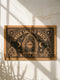 A rectangular coir doormat from Grimoire and Goblet featuring a central Eye of Providence within a Gothic arch. The text "UNDER SACRED WATCH" arcs above the design, while "NONE WITH ILL WILL ENTER" is horizontal. The design includes radiant sunburst lines, crescent moons, and eight-pointed stars. Symmetrical Art Nouveau botanicals and corner shields are printed in black on natural tan coconut fiber. This 24 by 16 inch threshold guardian warding mat has a black vinyl backing.