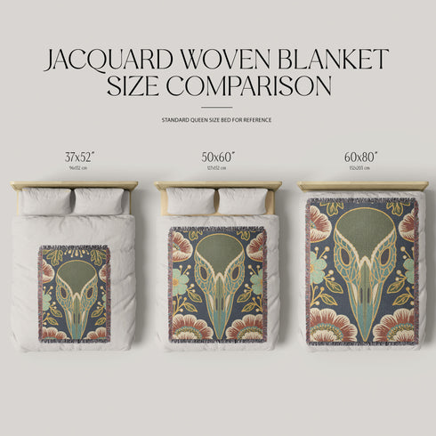 A midnight navy woven cotton blanket featuring a large central raven skull surrounded by rust and ochre flowers, and sage green ferns. Crescent moons are located in the four corners. The blanket has a colorful fringed edge and a textured, loomed appearance. Displayed as a premium gothic botanical home decor piece by Grimoire and Goblet.