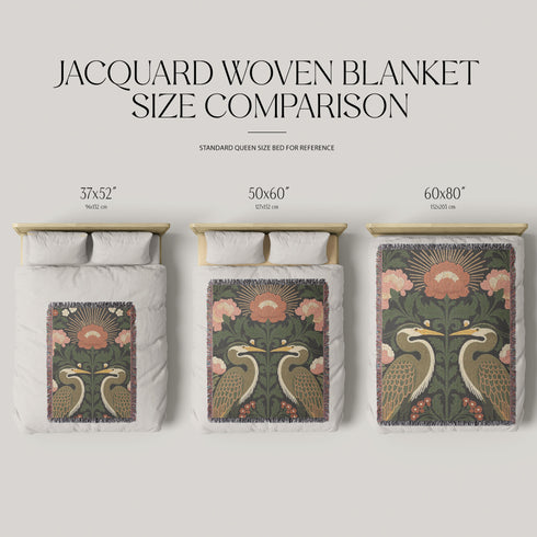 Jacquard woven cotton throw blanket, woven rather than printed, shown flat. Two mirrored great blue herons flank a central radial sunburst, surrounded by botanical blooms and scrollwork. The charcoal black ground carries antique gold ochre sunbeams, blush pink blossoms, deep forest green leaves, muted rust berry clusters, and cream toned herons. A lush multi-colored fringe of black, ochre, and sage threads edges the blanket, and the reverse shows an inverted charcoal grey version of the same design.
