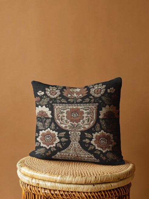 Woven tapestry pillow, 17" x 18", featuring an ornate chalice framed by botanical motifs in ivory, rust, and olive on a black ground. Artisan-woven of 58% cotton, 42% polyester and stuffed with soft, durable polyfill. Sewn shut for a smooth, seamless finish. Double-sided pattern for full visibility. Dark-academia, mystical décor accent; folklore-inspired woven pillow for sofa, chair, or bed.