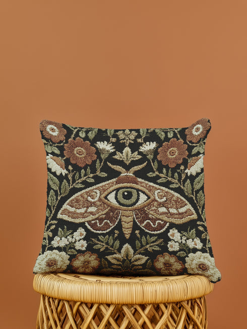 Woven tapestry pillow, 17" x 18", featuring a central moth with an eye and vintage florals in cream, rust, and olive on a black ground. Artisan-woven of 58% cotton, 42% polyester; stuffed with soft polyfill. Sewn-shut closure; double-sided pattern for full visibility. Botanical, symbolic woven pillow—folklore-inspired accent for couches, reading nooks, or beds.
