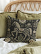 A premium, artisan-woven accent pillow from Grimoire and Goblet. The pillow is 17x18 and features a highly detailed, double-sided jacquard design on a deep black background. The artwork, woven in neutral gold, ecru, and muted olive threads, depicts a mystical, folkloric horse. This central horse figure is surrounded by a lush, symmetrical border of botanical flowers and leaves. The style is evocative of a medieval tapestry, perfect for dark academia, gothic, or arcane-themed decor.
