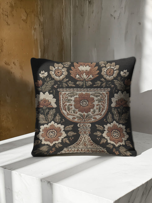 Woven tapestry pillow, 17" x 18", featuring an ornate chalice framed by botanical motifs in ivory, rust, and olive on a black ground. Artisan-woven of 58% cotton, 42% polyester and stuffed with soft, durable polyfill. Sewn shut for a smooth, seamless finish. Double-sided pattern for full visibility. Dark-academia, mystical décor accent; folklore-inspired woven pillow for sofa, chair, or bed.