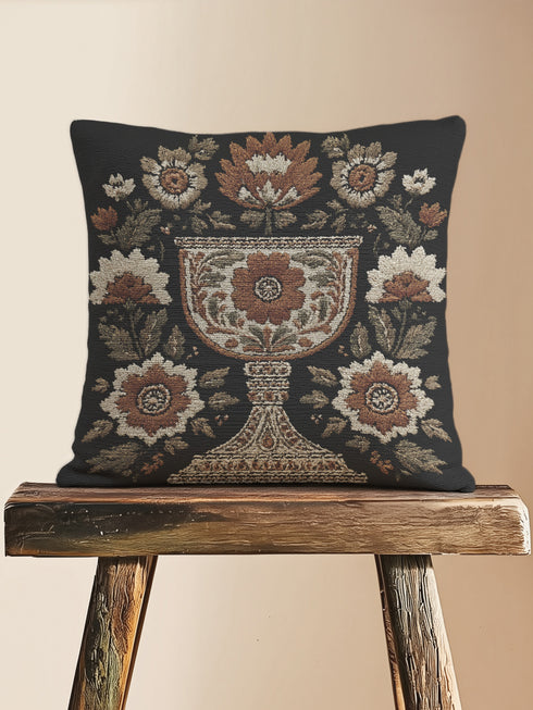 Woven tapestry pillow, 17" x 18", featuring an ornate chalice framed by botanical motifs in ivory, rust, and olive on a black ground. Artisan-woven of 58% cotton, 42% polyester and stuffed with soft, durable polyfill. Sewn shut for a smooth, seamless finish. Double-sided pattern for full visibility. Dark-academia, mystical décor accent; folklore-inspired woven pillow for sofa, chair, or bed.