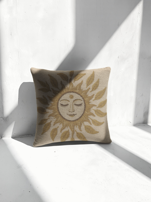 A square woven tapestry throw pillow in neutral earth tones of beige and gold. The pillow has a rich, textured surface from its jacquard weave. The design features a large, central celestial sun face with closed eyes, a serene smile, and a third eye symbol on its forehead. The sun's rays are stylized as intricate leaves, blending botanical and solar motifs. The pillow is made from a durable cotton and polyester blend, giving it a high-quality, artisanal feel.