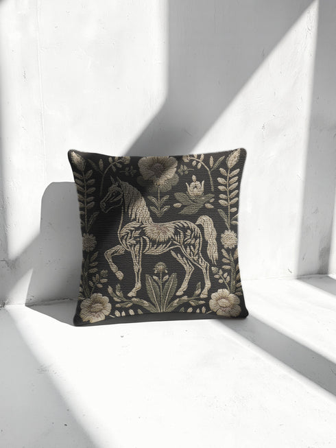 A premium, artisan-woven accent pillow from Grimoire and Goblet. The pillow is 17x18 and features a highly detailed, double-sided jacquard design on a deep black background. The artwork, woven in neutral gold, ecru, and muted olive threads, depicts a mystical, folkloric horse. This central horse figure is surrounded by a lush, symmetrical border of botanical flowers and leaves. The style is evocative of a medieval tapestry, perfect for dark academia, gothic, or arcane-themed decor.