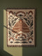 Grimoire and Goblet woven jacquard cotton blanket / wall tapestry featuring a centered folk-art moth framed by symmetrical wildflowers and leafy stems. Natural oatmeal-beige base with rust/terracotta and cocoa-brown moth detail, charcoal-black botanicals, and warm ivory highlights. Finished with a 2-inch multicolor fringe and a reversible color-negative back. Available in 52x37, 50x60, and 60x80 inches as a throw, bed cover, or statement wall hanging.