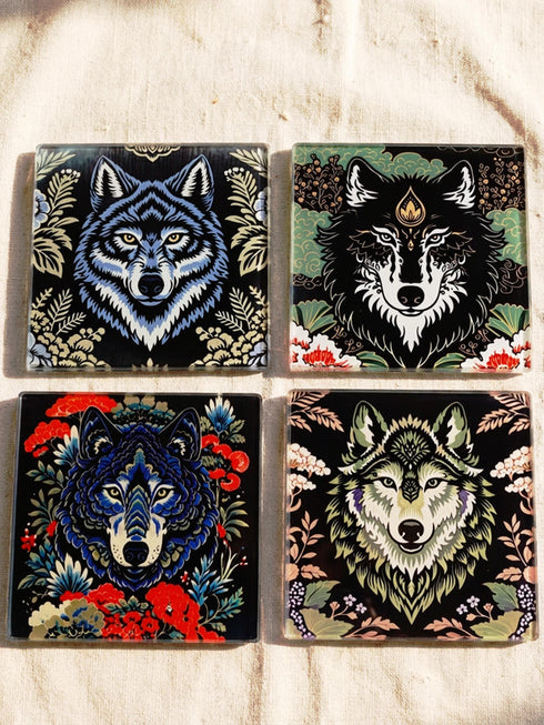 Set of 4 square tempered glass coasters featuring a mystical wolf design on a black background. High-gloss finish with non-slip rubber feet. Dark Academia and Whimsigoth aesthetic home decor. Close-up detail shows grey wolf fur texture and amber eyes. Durable drinkware protection for wooden tables. Grimoire and Goblet gothic luxury barware accessory for coffee tables and desks. Heat resistant glass surface with polished edges.