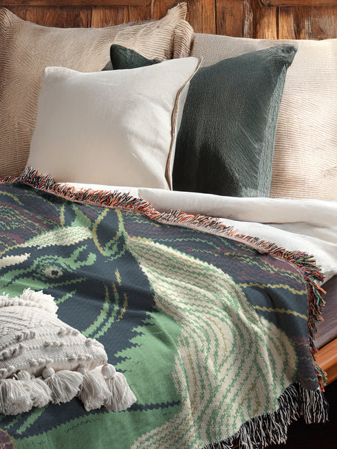 A Grimoire and Goblet woven cotton blanket featuring a large, stylized horse head in sage green and teal against a deep midnight navy background with wave patterns. The bottom edge features woven floral motifs in rust orange and deep plum. The design is a jacquard weave, not printed, with visible thread texture and multi-colored fringe edges. Chinoiserie and Art Nouveau style equestrian tapestry throw.