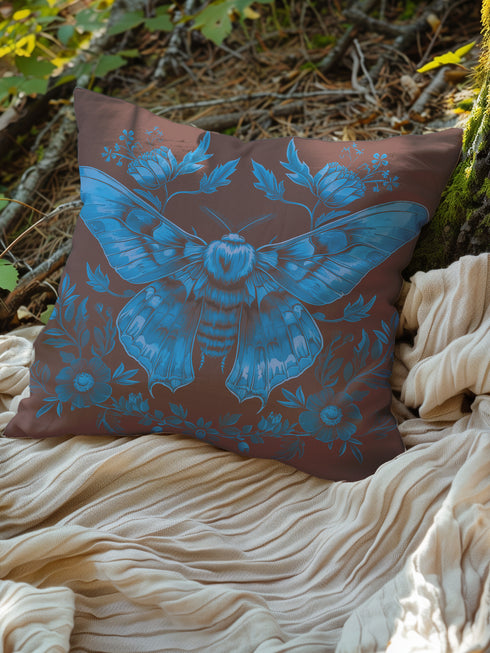 A decorative pillow cover featuring a large Luna moth illustration in electric blue on a rich chocolate brown background, adorned with symmetrical botanical elements and flowers in a detailed vintage naturalist style.
