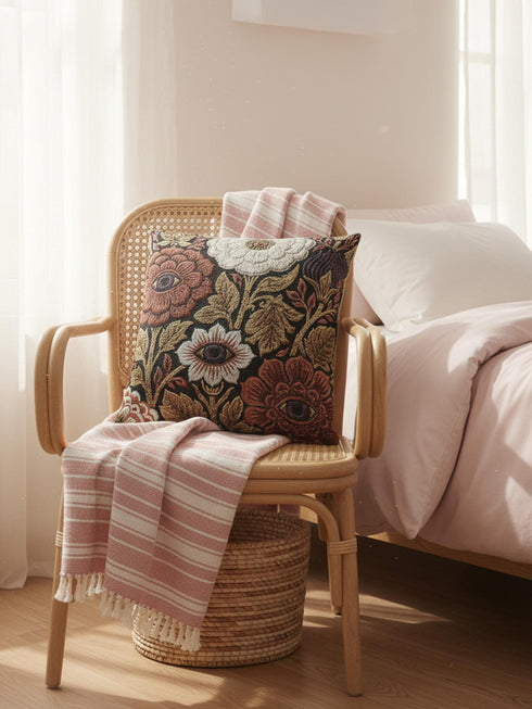 A square woven throw pillow featuring a surreal botanical design on a solid black background. The tapestry-style fabric showcases large, detailed flowers in shades of rust red, cream, and olive green. Nestled within the center of each prominent blossom is a detailed, human-like eye with a dark plum iris, creating a striking evil eye motif. The interwoven threads give the pillow a rich, textured appearance. The pillow is fully stuffed and sewn closed, presenting a smooth, seamless edge.