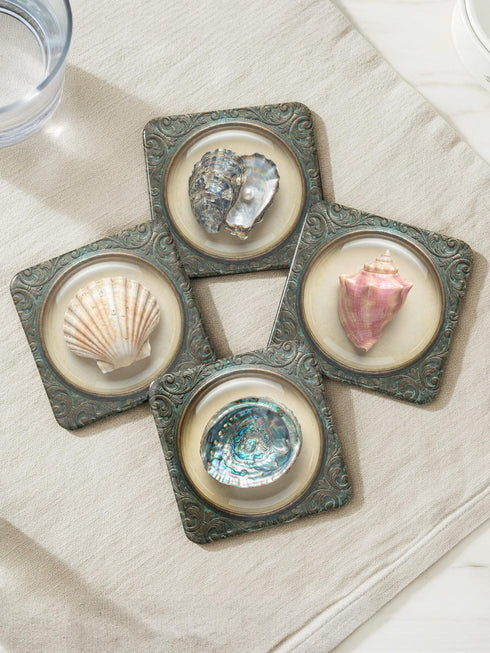 A high-fidelity 2D Trompe-l’œil print on a set of four 4x4 inch square coasters. Each coaster features a centralized sea specimen—a scallop, an oyster with a pearl, a pink conch, and an abalone—centered within an ornate, circular Victorian scrollwork frame. The design uses a faux-texture effect to mimic raised bronze and verdigris metal. The colors include aged gold, teal, and cream, creating a vintage museum specimen aesthetic