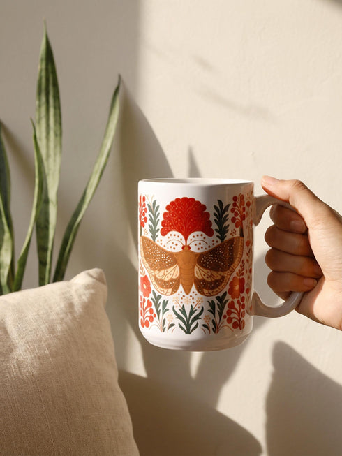 A detailed close-up of a luxury ceramic mug and matching square coaster set from Grimoire and Goblet. The items feature a vintage-style scientific illustration of a large moth with intricate wing patterns in earth tones of rust red and moss green, resting on stylized botanical foliage. The aesthetic is Dark Academia and Victorian Gothic. The mug is a large 15oz white ceramic vessel with a sturdy C-handle. The coaster is a glazed ceramic tile with a glossy finish.