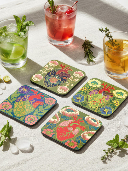 A set of four premium 4x4 inch anatomical heart coasters from Grimoire and Goblet. Each square coaster is made of masonite hardboard with a high-gloss finish and a non-slip cork base. The designs feature intricate biological heart illustrations with folk-art floral motifs in vibrant crimson, pink, yellow, and purple against mossy green and deep teal backgrounds. The high-fidelity print mimics a luxury embroidered texture, perfect for a cardiology gift or dark academia home decor.