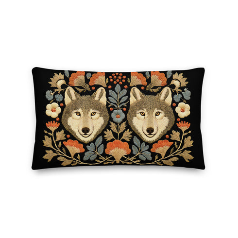 A rectangular black lumbar pillow, 12x20 inches, with a detailed symmetrical folk art print. The design features two forward-facing grey wolf heads in the center, flanked by intricate botanical elements. The color palette is moody and rustic, with flowers in burnt orange and cream, and leaves in slate blue and antique gold. The artwork has a faux embroidery, tapestry-style texture. This woodland animal accent cushion is made from a premium polyester fabric with a soft, linen feel.