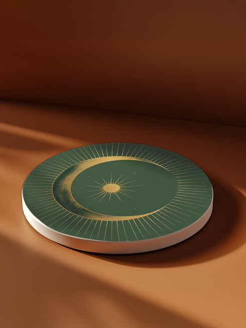 Round ceramic coaster with forest green background. Golden crescent moon embraces a sun at the center. Fine golden lines radiate outward, creating a sunburst pattern to the edge. White rim indicates cork backing. Coaster diameter is 4.04 inches.