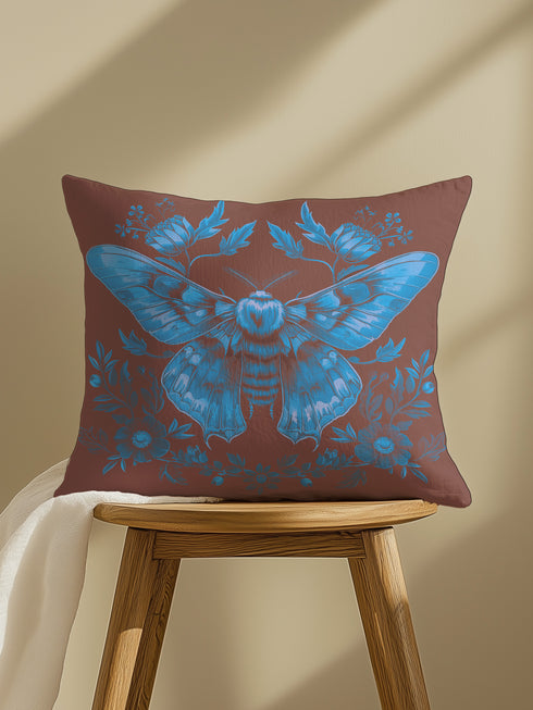 A decorative pillow cover featuring a large Luna moth illustration in electric blue on a rich chocolate brown background, adorned with symmetrical botanical elements and flowers in a detailed vintage naturalist style.