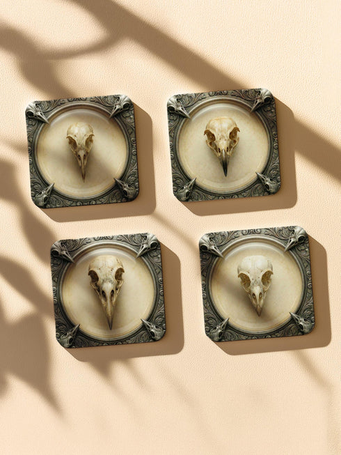 A set of four square 4x4 inch coasters by Grimoire and Goblet. Each features a unique avian skull specimen: a hooked raptor, a slender insectivore, a straight-billed corvid, and a scavenger. Designs are framed by silver faux-texture scrollwork on aged parchment. The coasters have a reflective high-gloss finish and tan cork backing. A perfect companion for a gothic goblet or grimoire study.