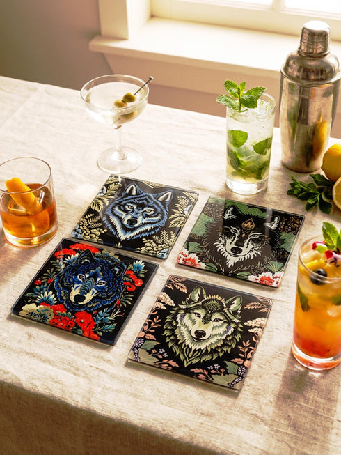 Set of 4 square tempered glass coasters featuring a mystical wolf design on a black background. High-gloss finish with non-slip rubber feet. Dark Academia and Whimsigoth aesthetic home decor. Close-up detail shows grey wolf fur texture and amber eyes. Durable drinkware protection for wooden tables. Grimoire and Goblet gothic luxury barware accessory for coffee tables and desks. Heat resistant glass surface with polished edges.