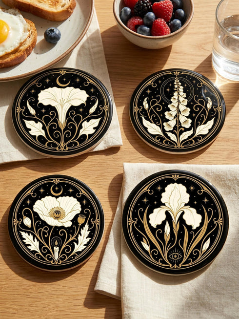 A set of four round 4-inch ceramic coasters featuring a glossy 2D flat-printed Art Deco botanical design. Each coaster displays a different cream-colored flower including a moonflower, foxglove, poppy, and iris, set against a solid black background. The floral motifs are framed by intricate gold linework, crescent moons, four-pointed stars, and mystical symbols like a candle and an all-seeing eye. The coasters have a smooth white edge and are finished with a natural brown cork backing.