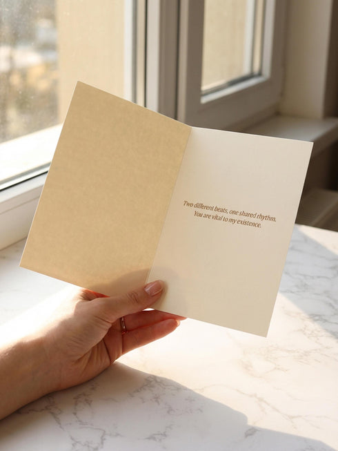 A vintage-style greeting card titled "DE HUMANI CORDIS" featuring a medical illustration of two anatomical hearts connected by a single looped blood vessel. The hearts are drawn in a sepia and crimson woodcut style on a cream background mimicking aged parchment. Text below reads "Fig. 14: The Twin Pulse." The card evokes a dark academia or cottagecore aesthetic. Inside text reads "Two different beats, one shared rhythm.