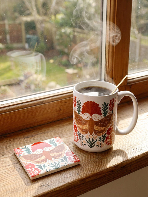 A detailed close-up of a luxury ceramic mug and matching square coaster set from Grimoire and Goblet. The items feature a vintage-style scientific illustration of a large moth with intricate wing patterns in earth tones of rust red and moss green, resting on stylized botanical foliage. The aesthetic is Dark Academia and Victorian Gothic. The mug is a large 15oz white ceramic vessel with a sturdy C-handle. The coaster is a glazed ceramic tile with a glossy finish.