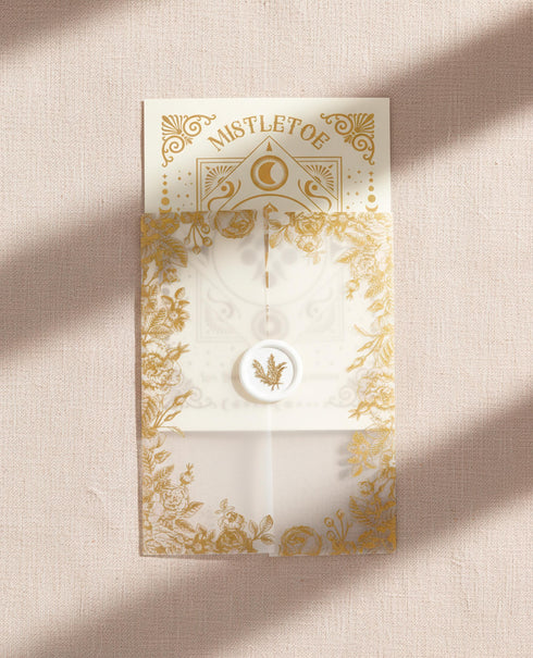 A Grimoire & Goblet luxury Mistletoe ritual card set. The 5x7 cream greeting card features gold celestial designs framing “Mistletoe” and “Love, Protection & New Beginnings.” Shown with a vellum wrap printed in gold florals, a white wax seal with mistletoe, and a premium envelope. Includes a 4x6 ritual insert on handmade deckled paper titled “Ritual for Peace and Protection.” A spiritual Yule stationery set designed as a luxurious unboxing experience.